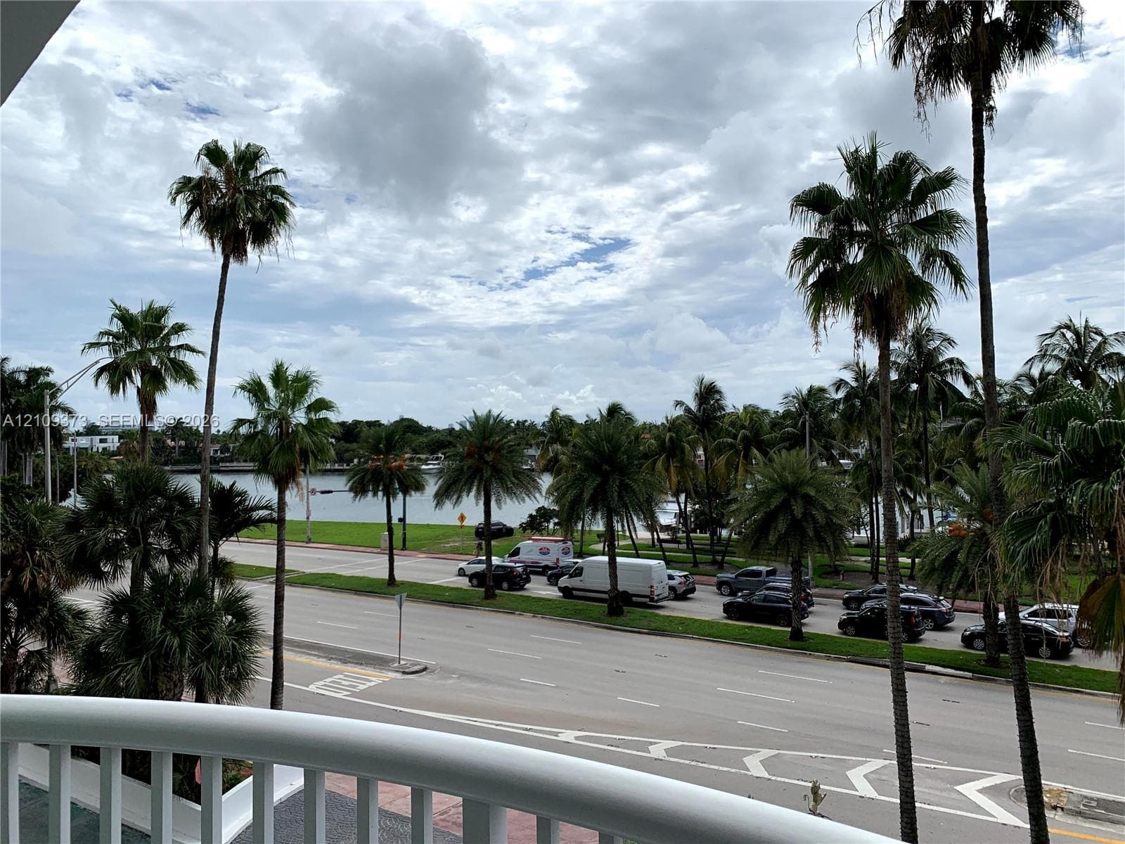 Exterior balcony featuring a white railing and a backdrop of mature palm trees overlooking a waterway