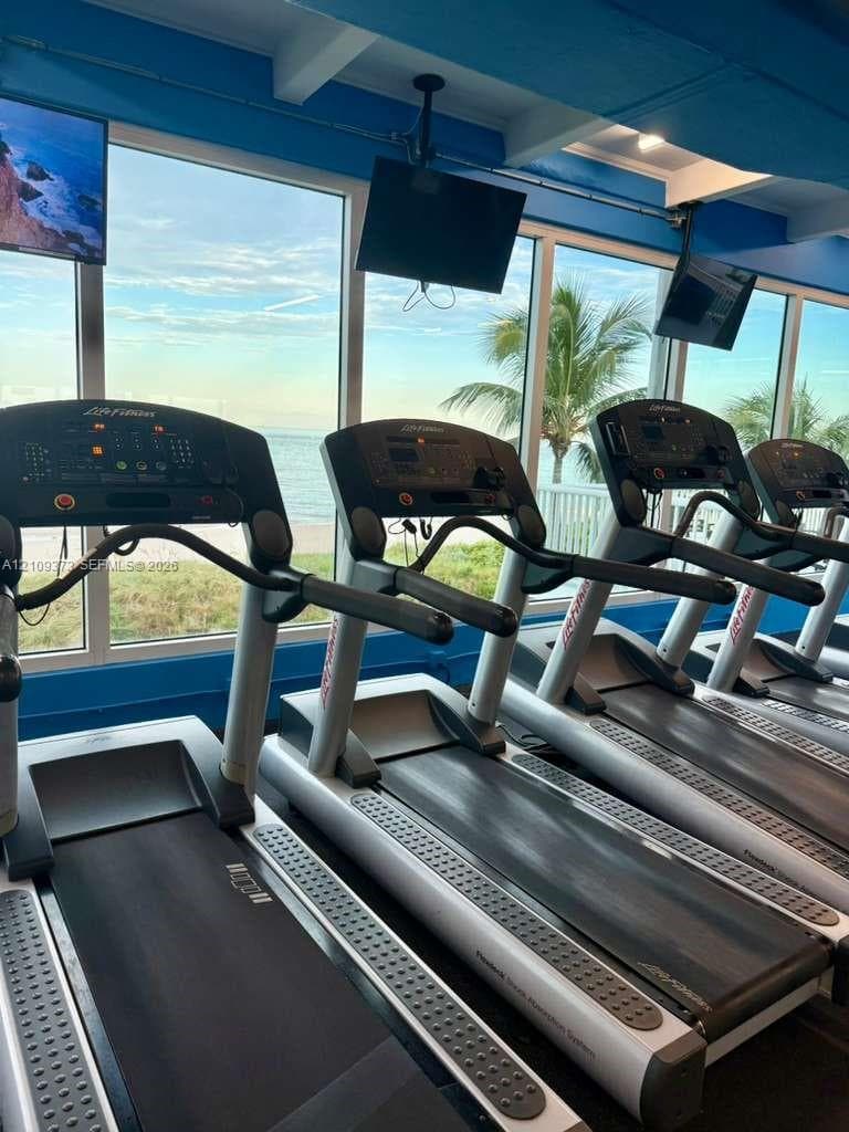 Fitness center featuring floor-to-ceiling windows, ocean horizon exposure, and ceiling-mounted televisions