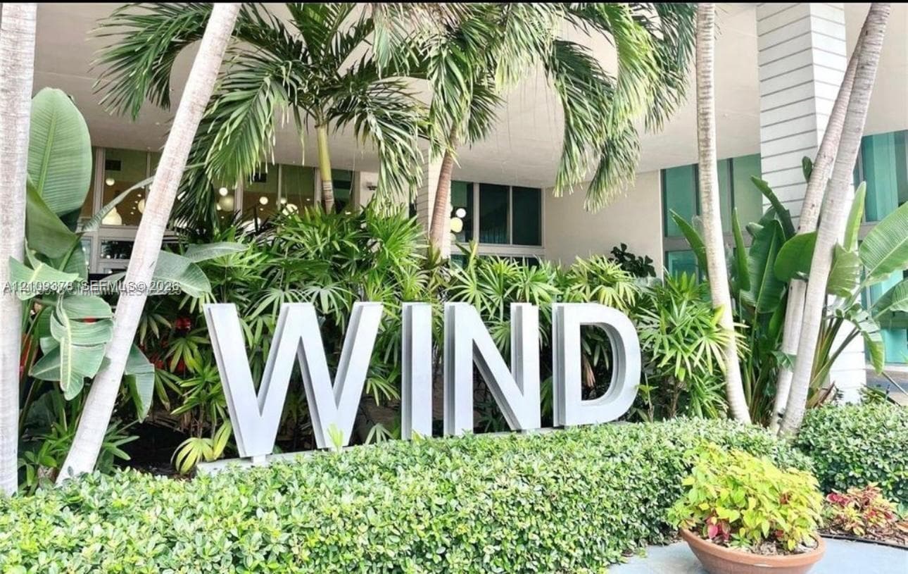 Exterior building signage featuring dimensional lettering nestled within mature tropical landscaping, including palm trees and manicured shrubbery
