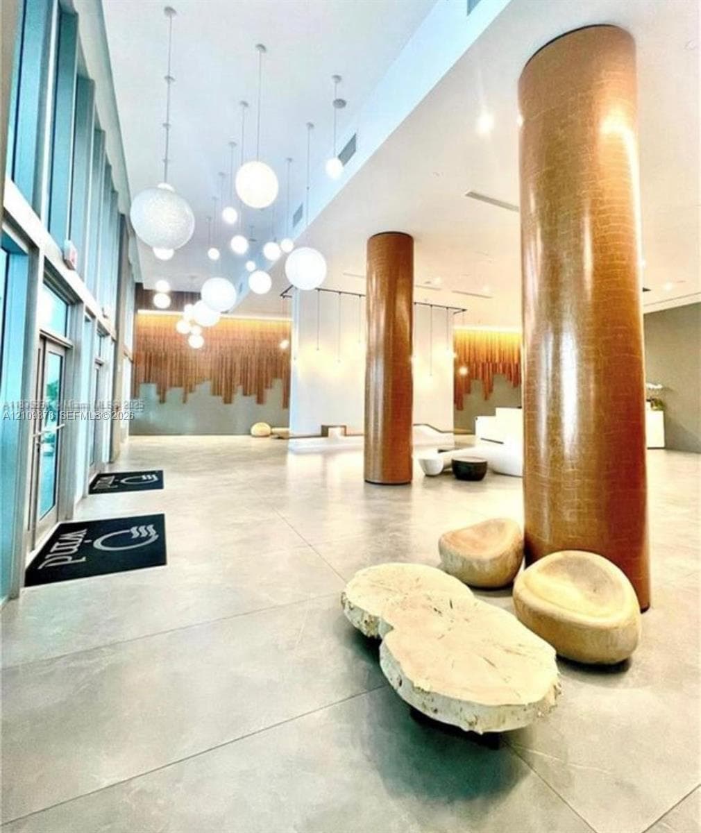 Grand lobby entrance featuring high ceilings, floor-to-ceiling windows, polished stone flooring, custom pendant globe lighting, and textured metallic-finish structural columns