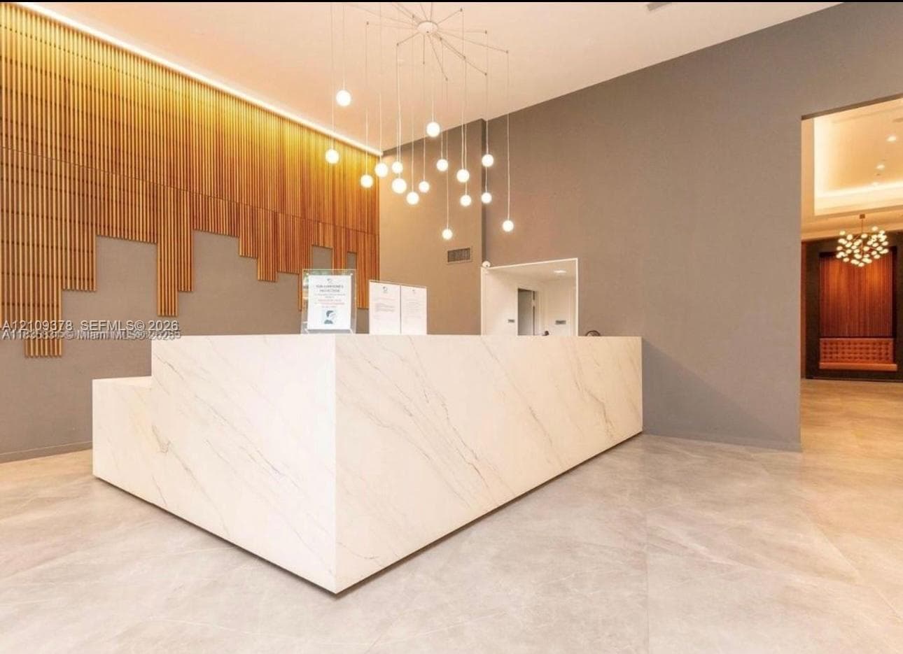 Reception area featuring a stone-finish desk, vertical slat wood wall paneling, large-format tile flooring, and a multi-bulb pendant chandelier