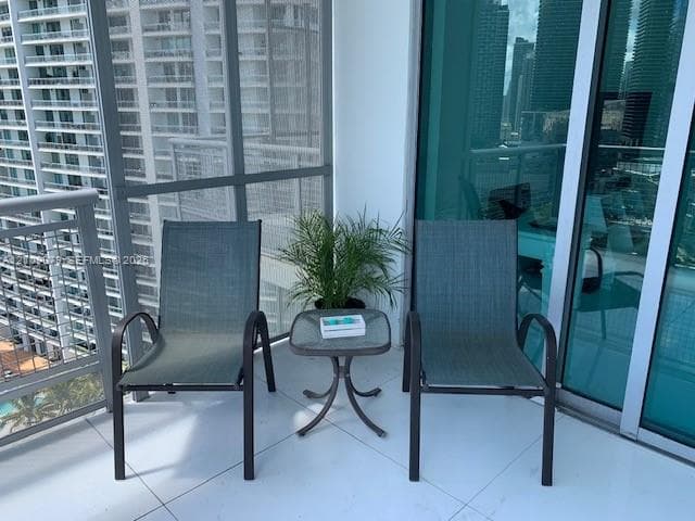 Covered balcony featuring white tile flooring, metal railings, and floor-to-ceiling glass paneling