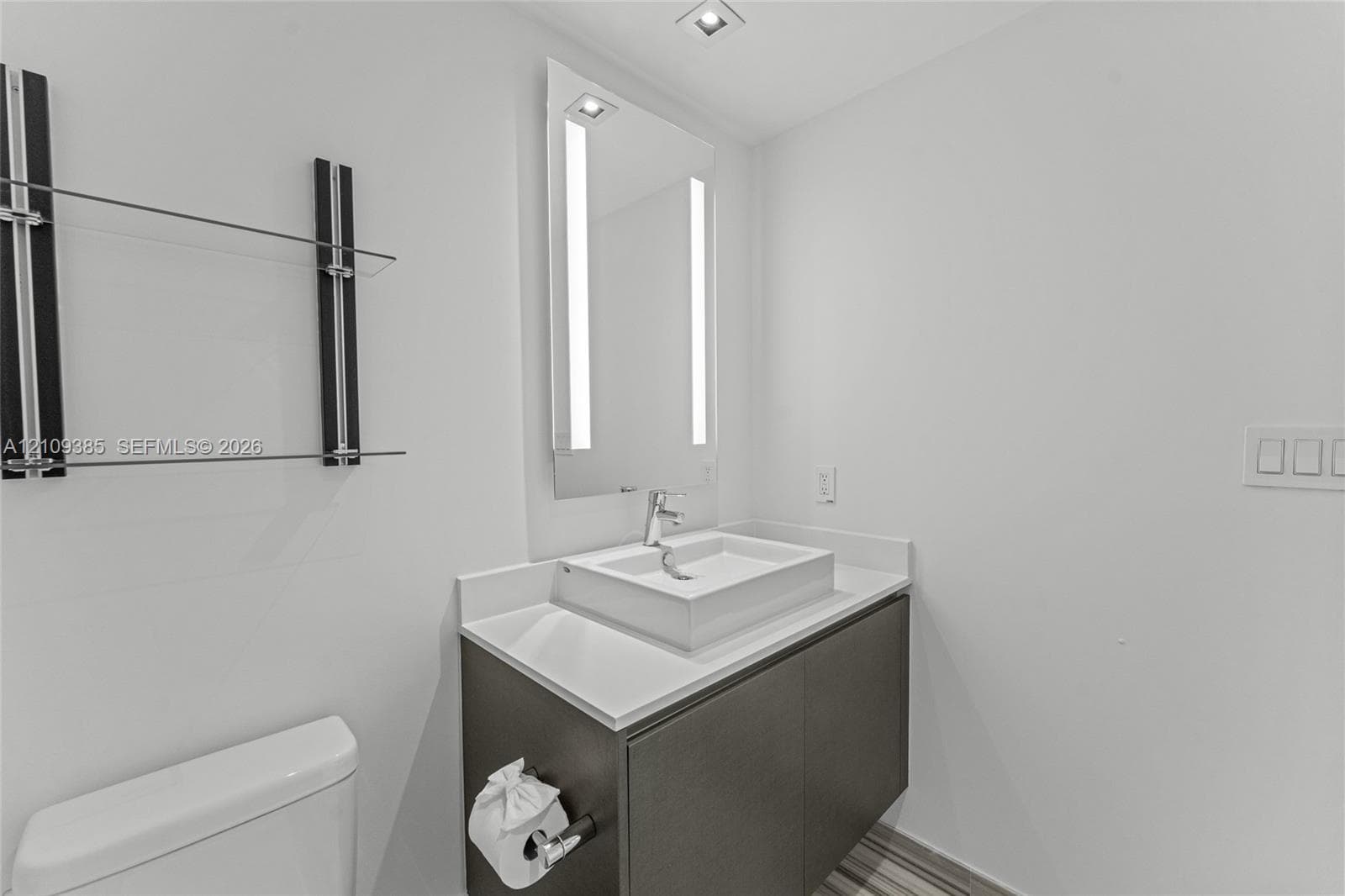 Floating vanity with a solid-surface countertop and rectangular vessel sink, integrated LED mirror, and wall-mounted glass shelving