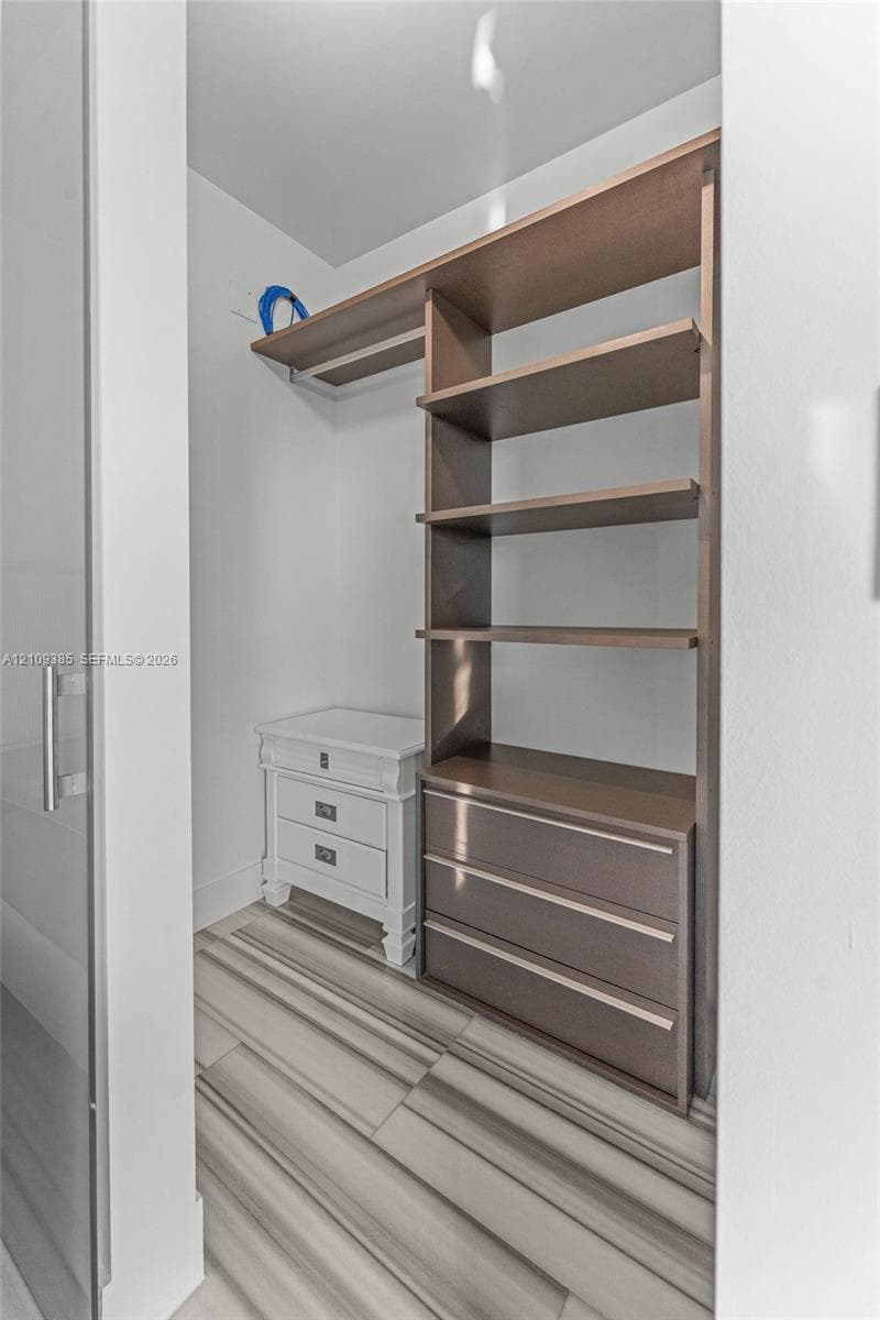 Walk-in storage space featuring wood-finish open shelving, built-in lower drawers, and tile flooring