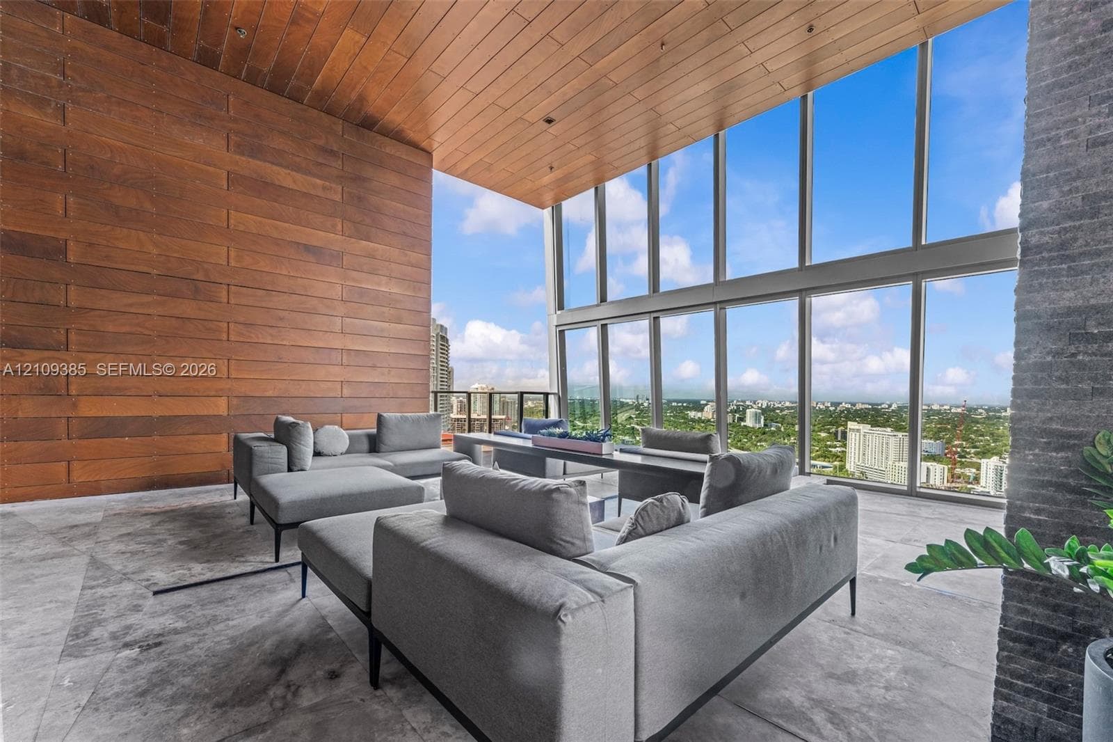 Covered loggia featuring floor-to-ceiling windows, wood-paneled ceiling, stone flooring, and a textured stone pillar