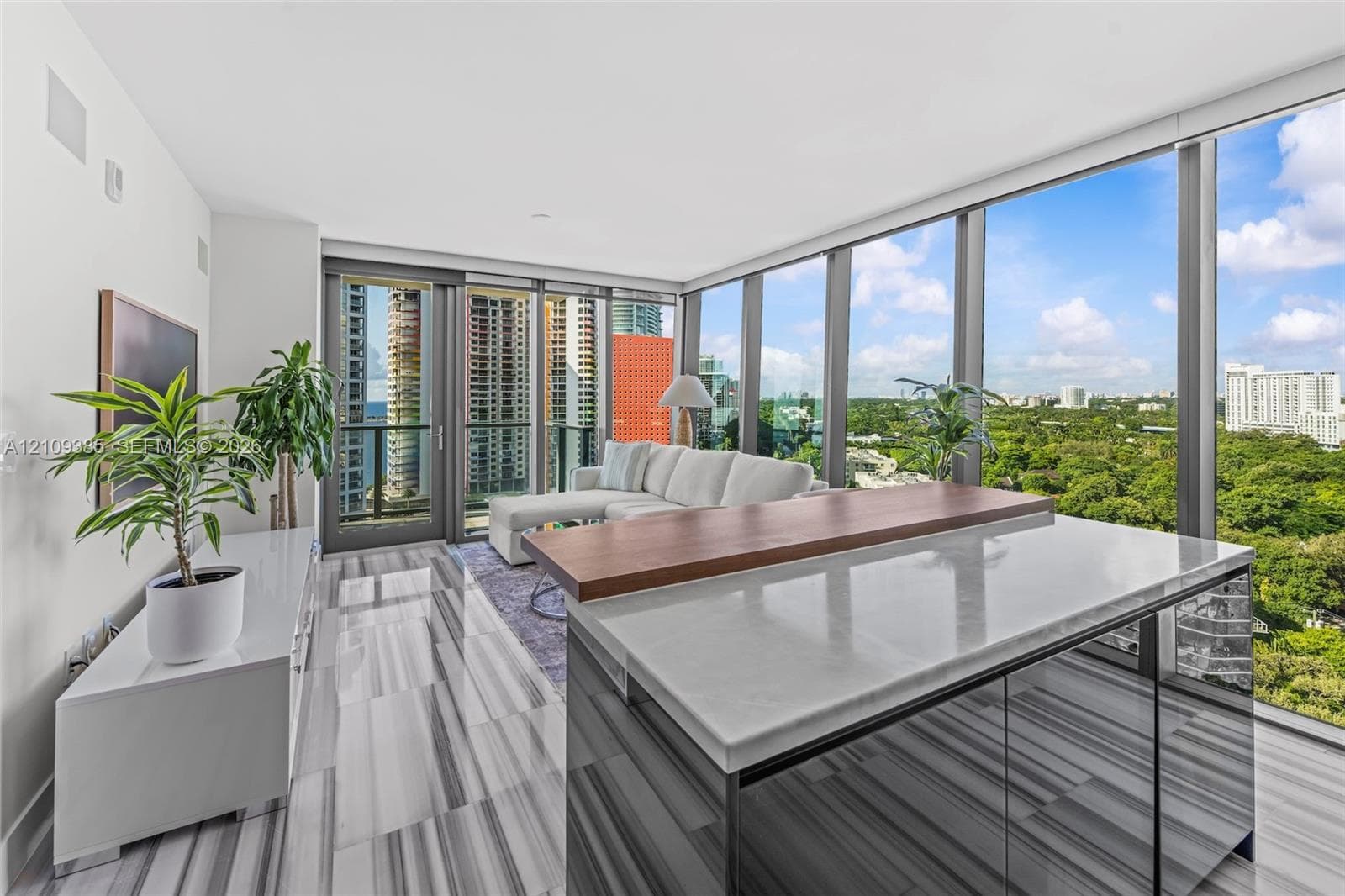 Floor-to-ceiling windows, kitchen island with stone countertop and raised wood-finish bar, and light-toned tile flooring