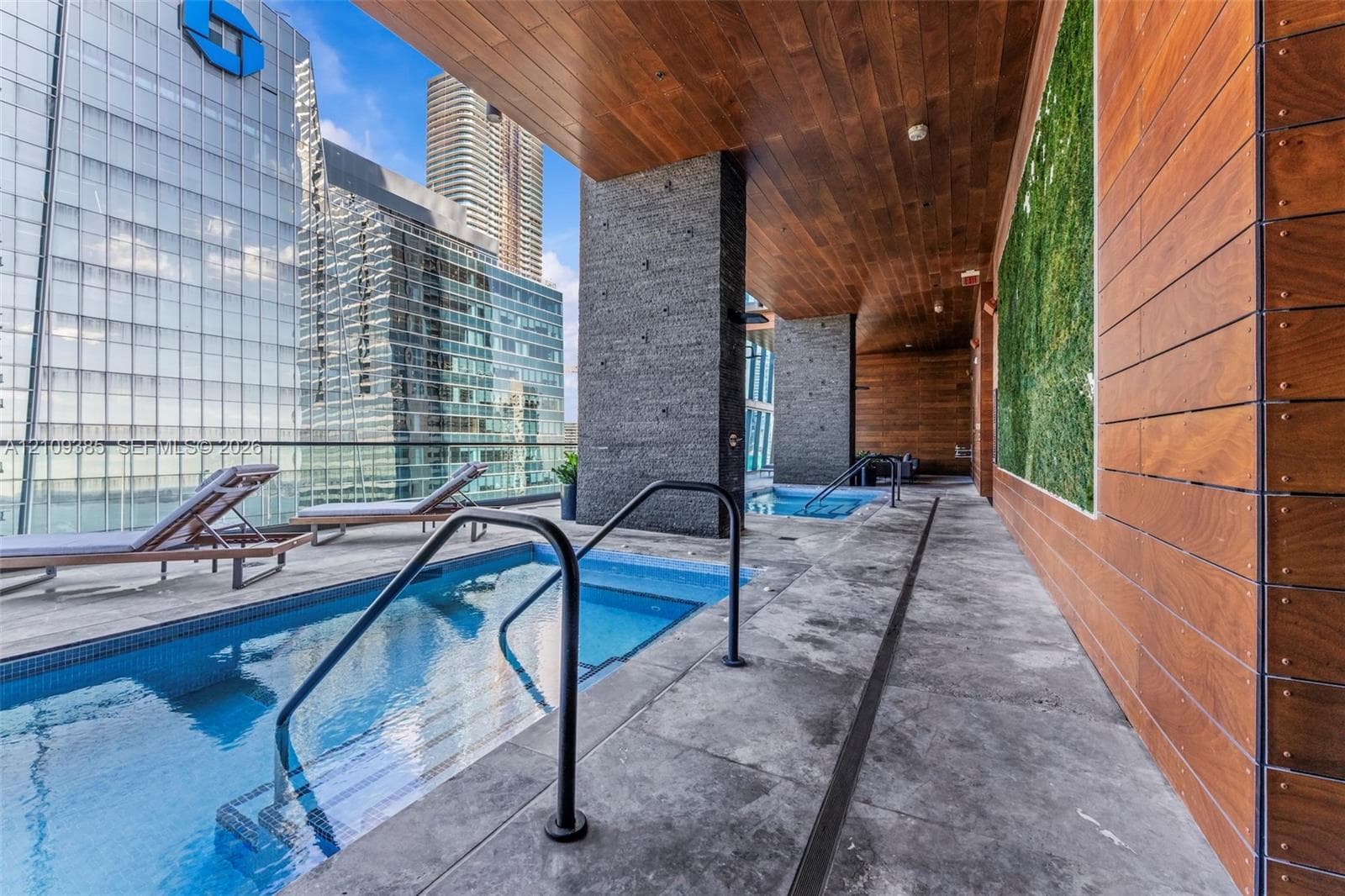 Covered terrace featuring a lap pool, secondary dipping pool, wood-paneled ceiling, stone flooring, and a vertical greenery wall