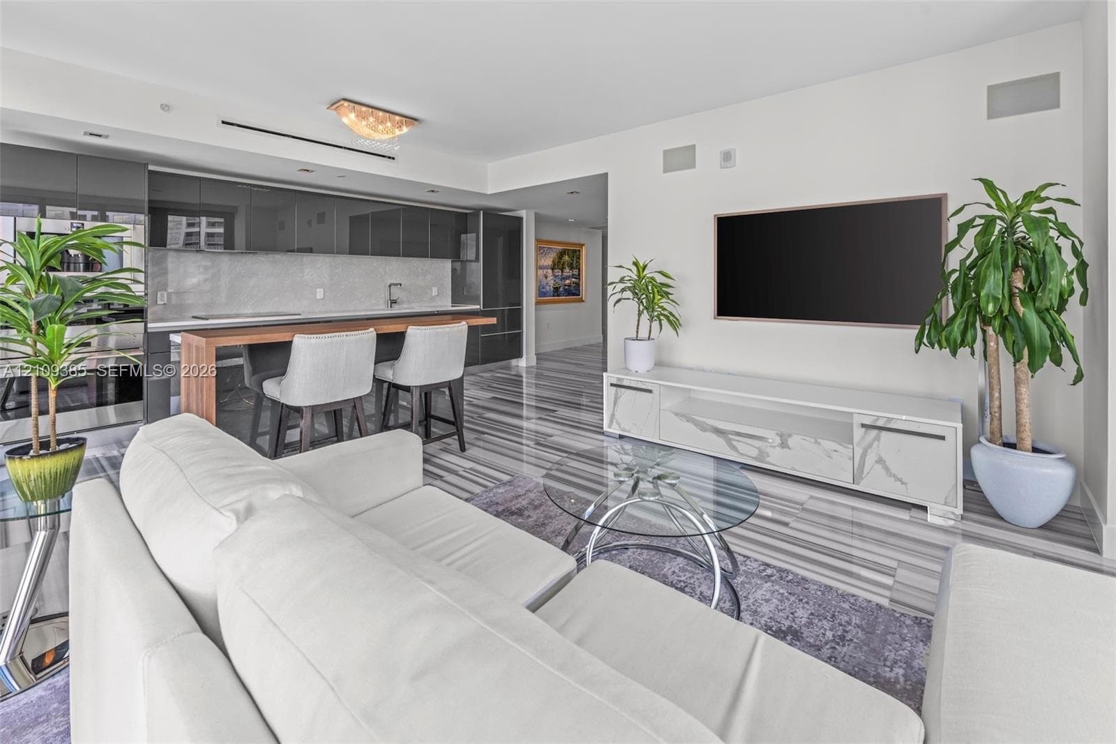 Kitchen featuring high-gloss cabinetry, stone backsplash, and an integrated wood-finish breakfast bar, complemented by polished stone-finish flooring throughout the main area
