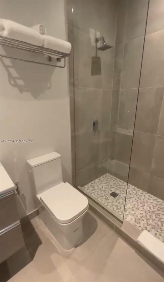 Glass-enclosed shower with pebble tile flooring, wall-mounted rainfall showerhead, and polished chrome fixtures