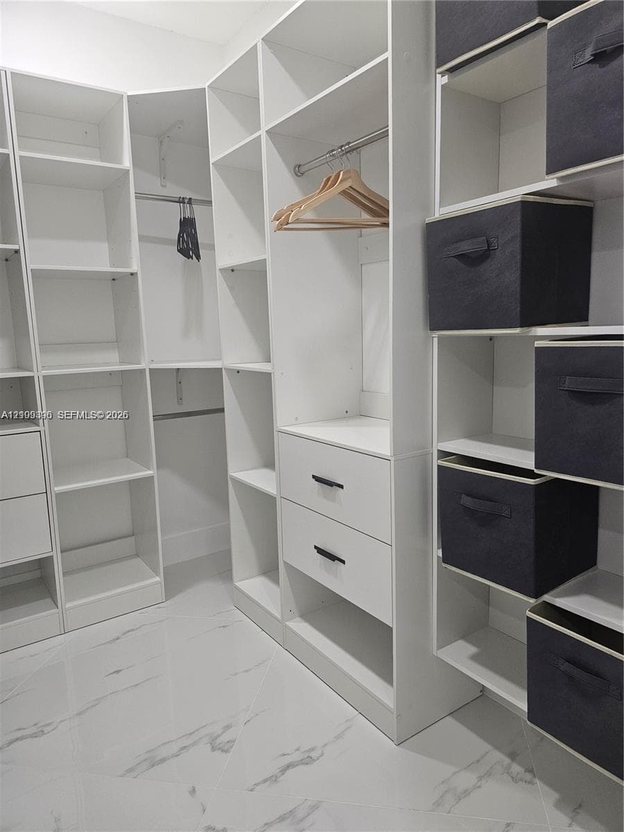 Custom reach-in closet featuring white floor-to-ceiling built-in shelving, integrated hanging rods, two soft-close drawers with matte black hardware, and polished stone-finish flooring