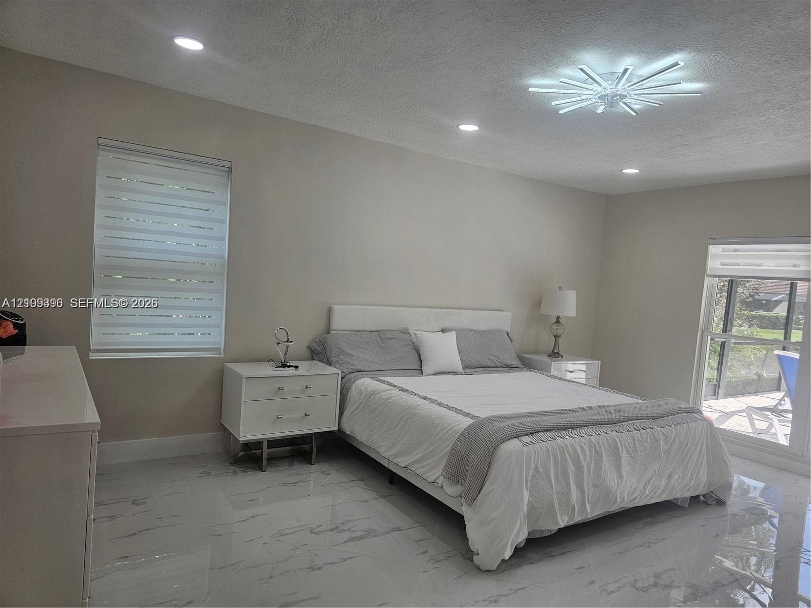 Polished stone-finish tile flooring, modern starburst ceiling fixture, recessed lighting, and dual windows with integrated shades