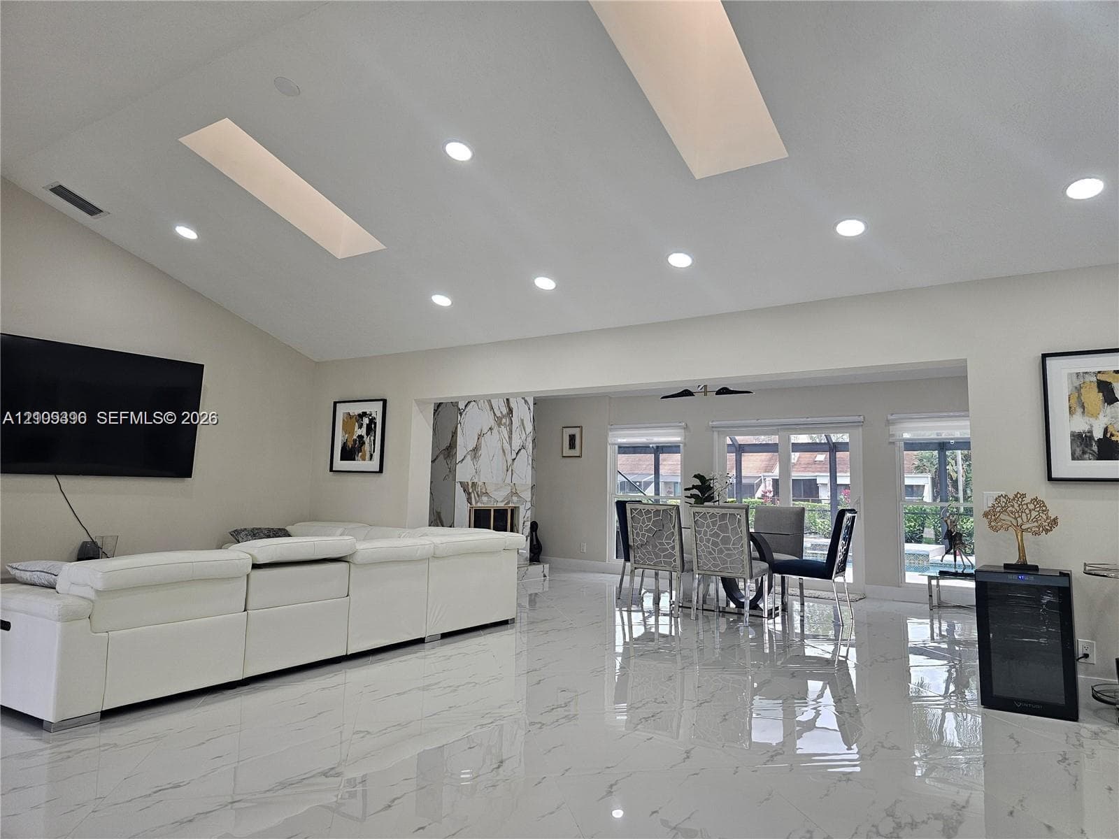 Vaulted ceilings featuring dual skylights, recessed lighting, polished stone-finish flooring, and a floor-to-ceiling stone-surround fireplace