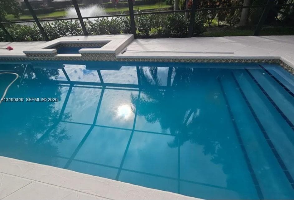 Screened-in pool area featuring an integrated spa, tiled waterline finish, and concrete pool deck