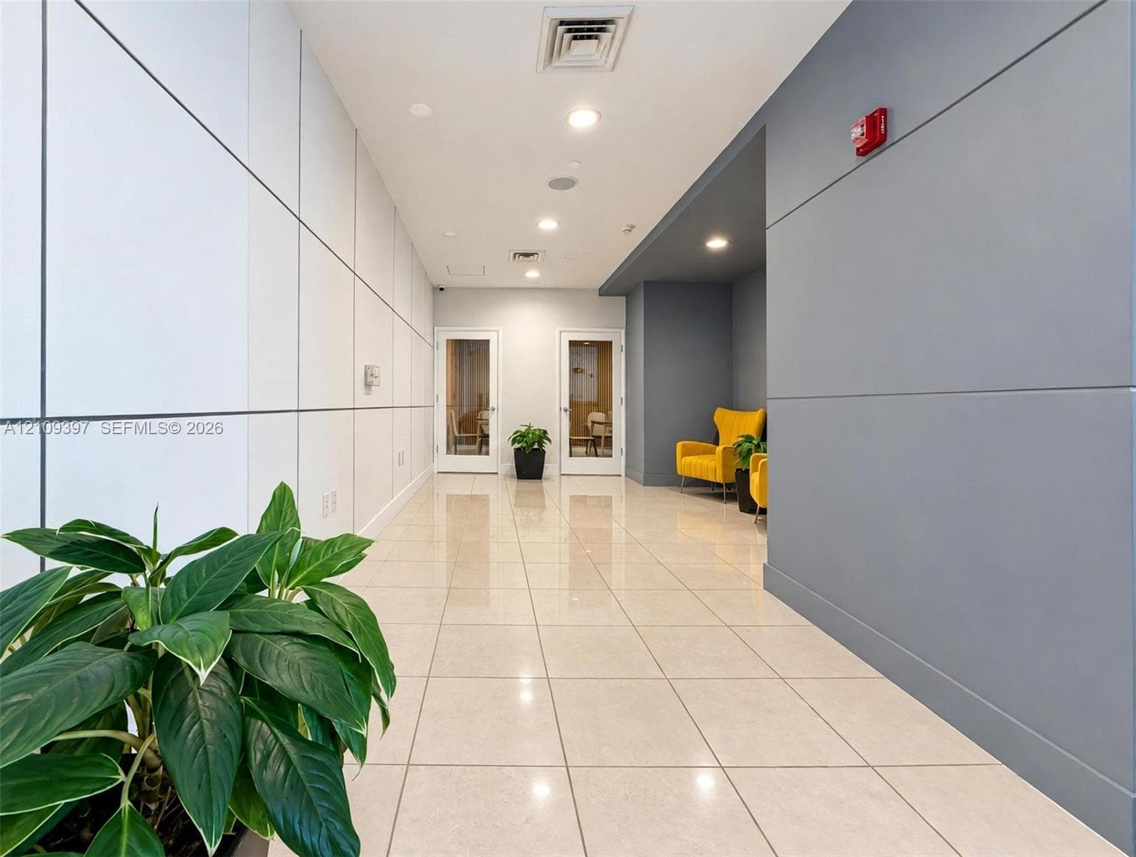 Contemporary corridor featuring large-format light tile flooring, white panel wall detailing, recessed ceiling lighting, and a contrasting charcoal-colored accent wall