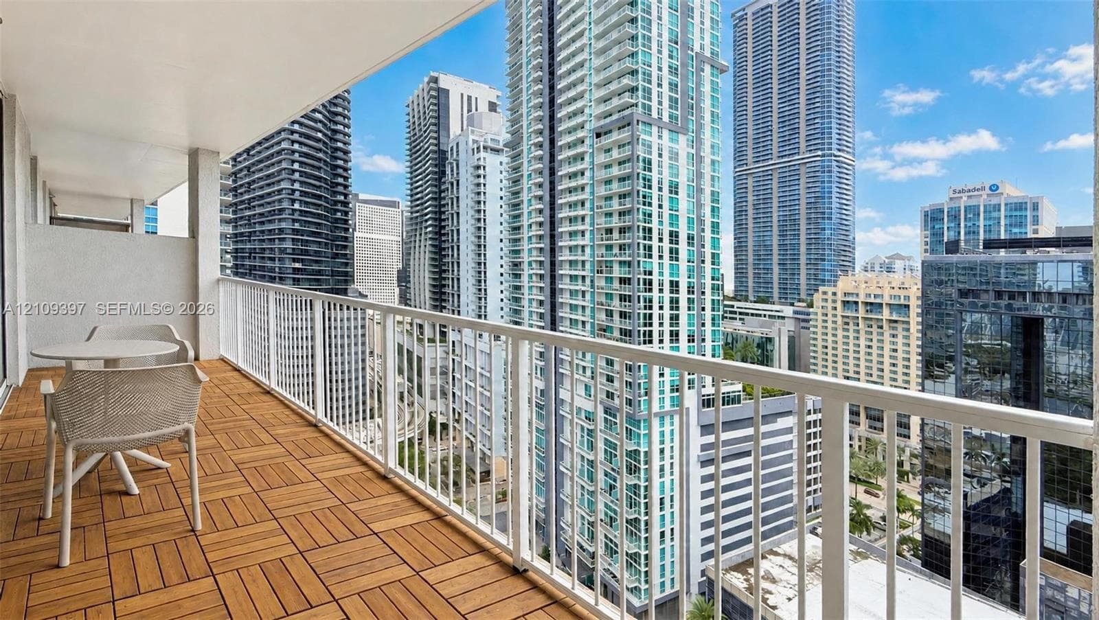 Private balcony featuring wood-finish decking, white metal railing, and high-rise urban surroundings