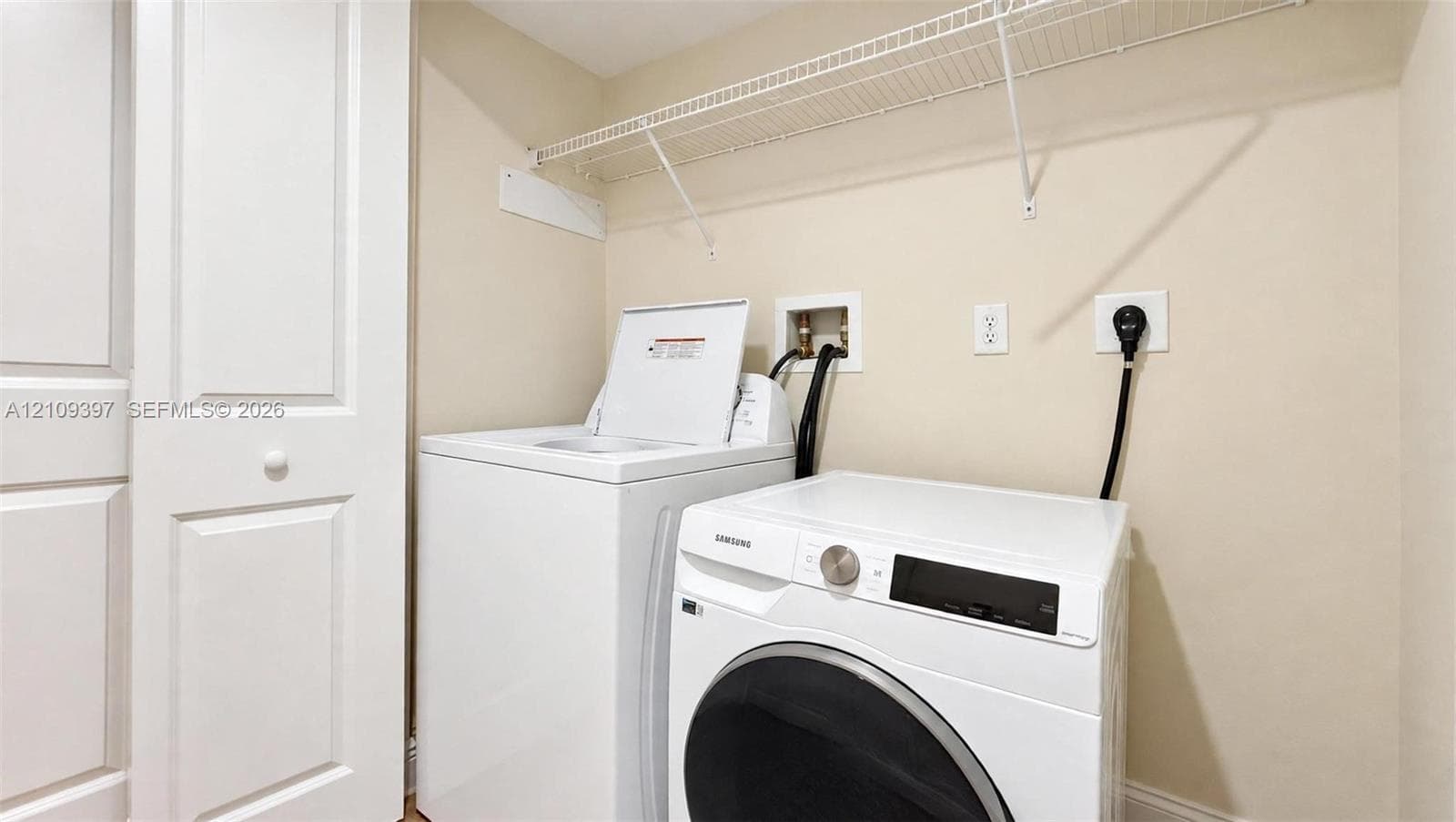 Laundry area featuring built-in shelving, white paneled door, and recessed utility hookups