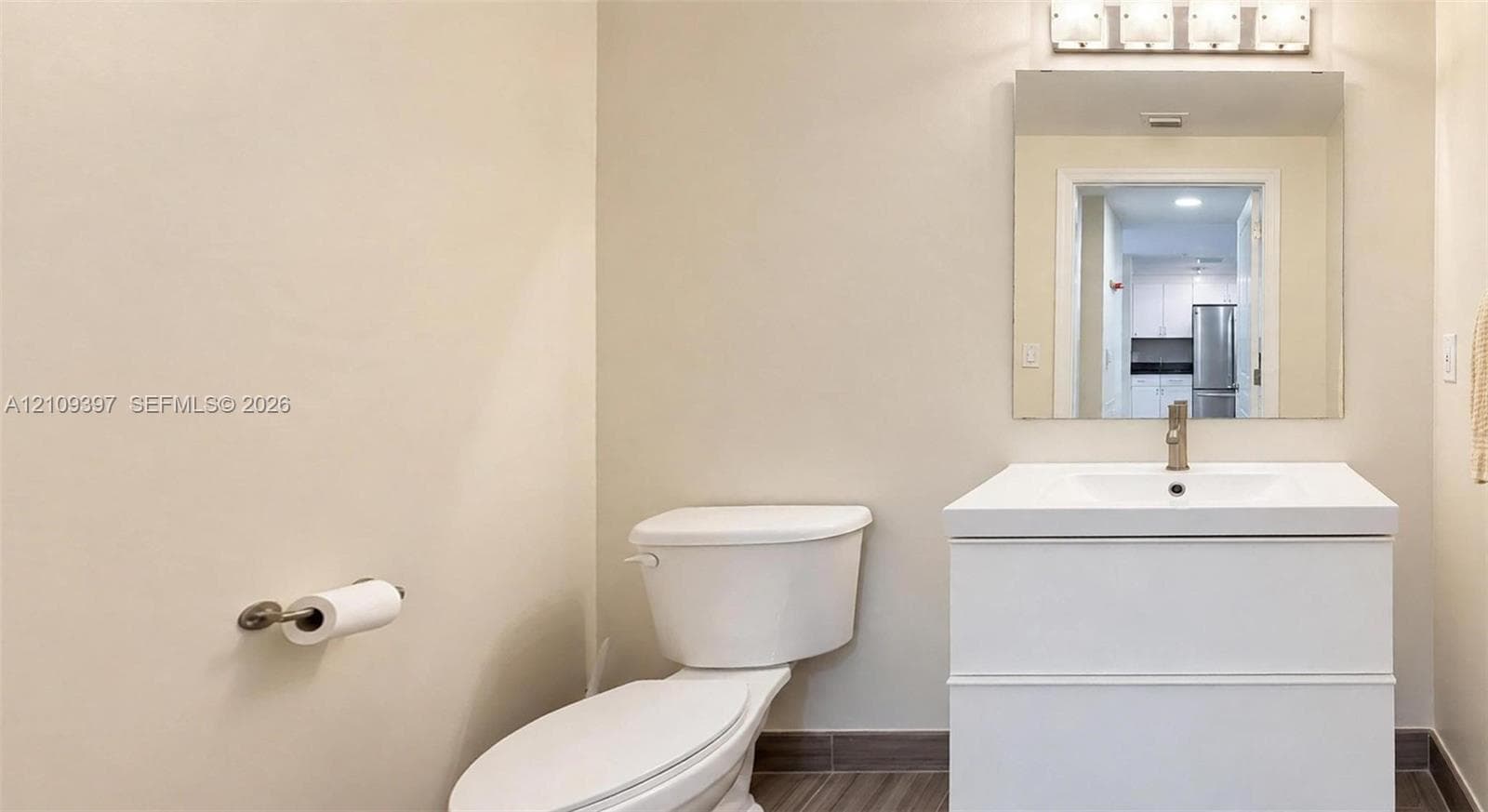 White vanity with integrated rectangular sink and polished chrome faucet, rectangular wall-mounted mirror, four-light vanity fixture, and neutral-tone tile flooring