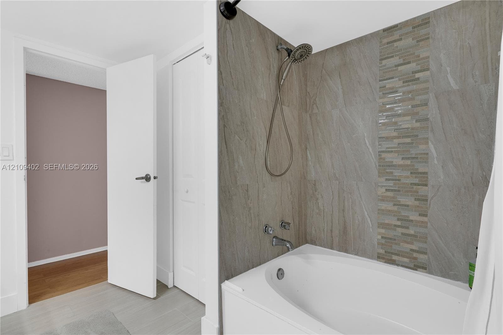 Bathtub featuring a tiled surround with stone-finish panels, vertical mosaic accent inlay, handheld showerhead, and wall-mounted faucet