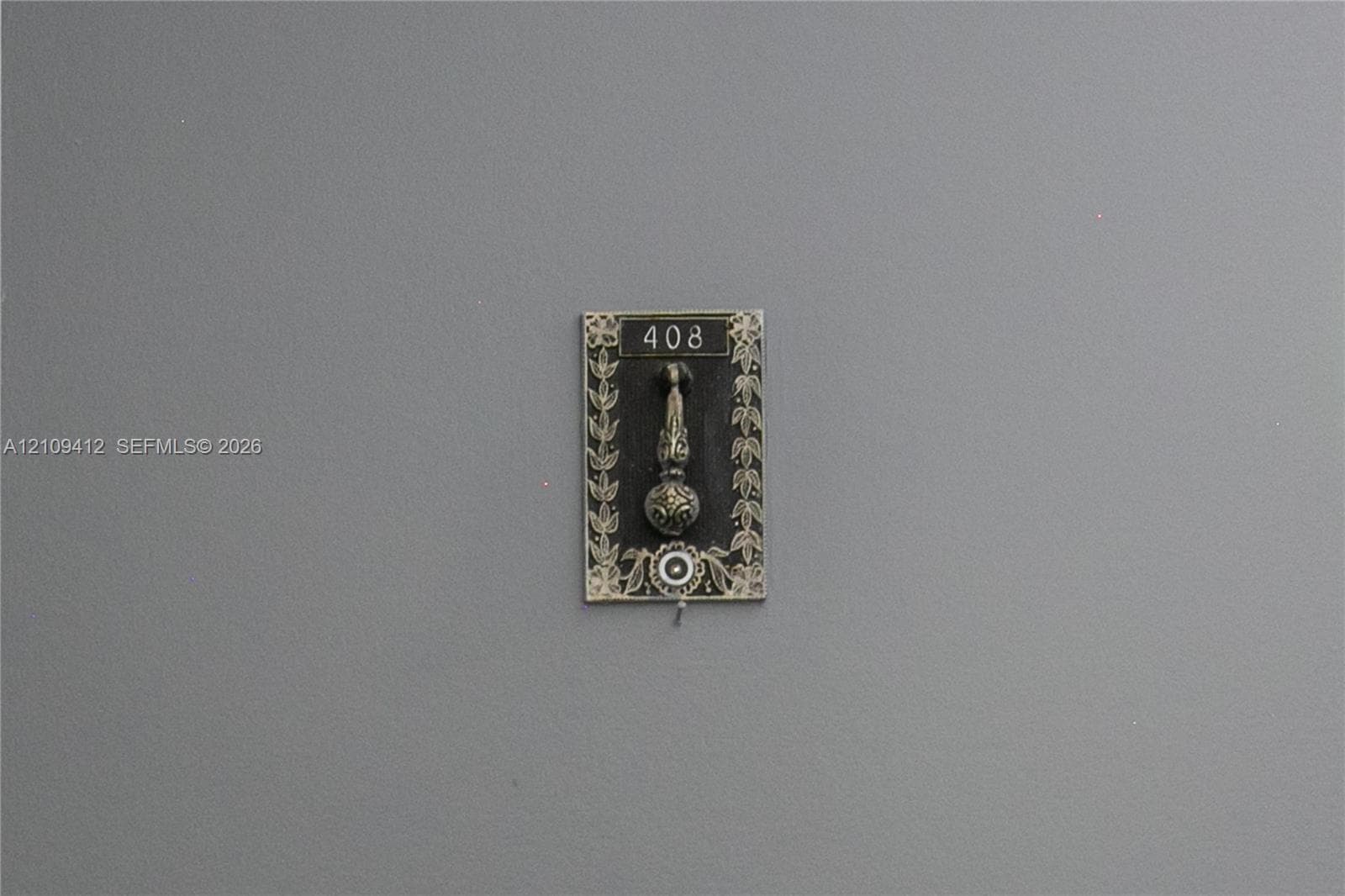 Decorative metal door knocker featuring an ornate floral border, engraved numbering, and a circular accent detail