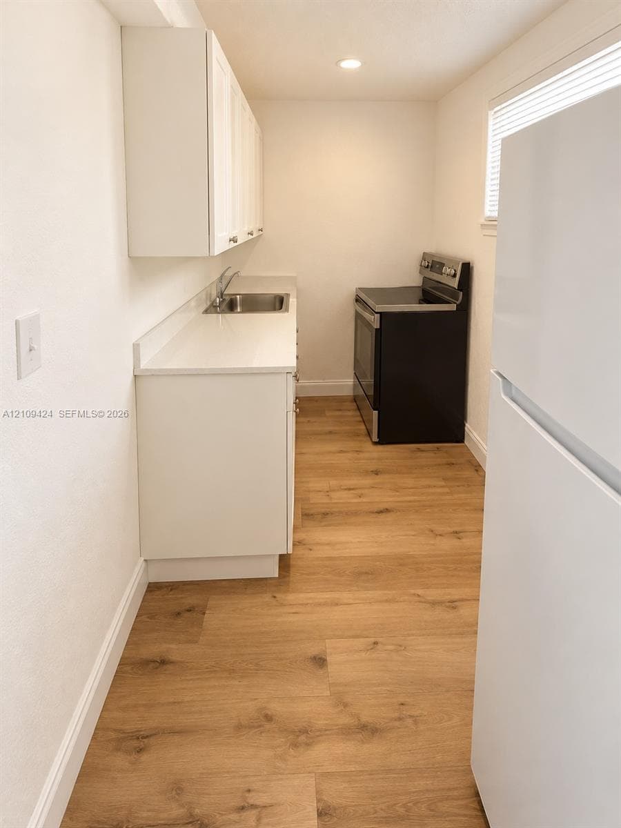 Galley kitchen featuring white cabinetry, solid-surface countertops, stainless steel sink, wood-finish flooring, and recessed ceiling lighting