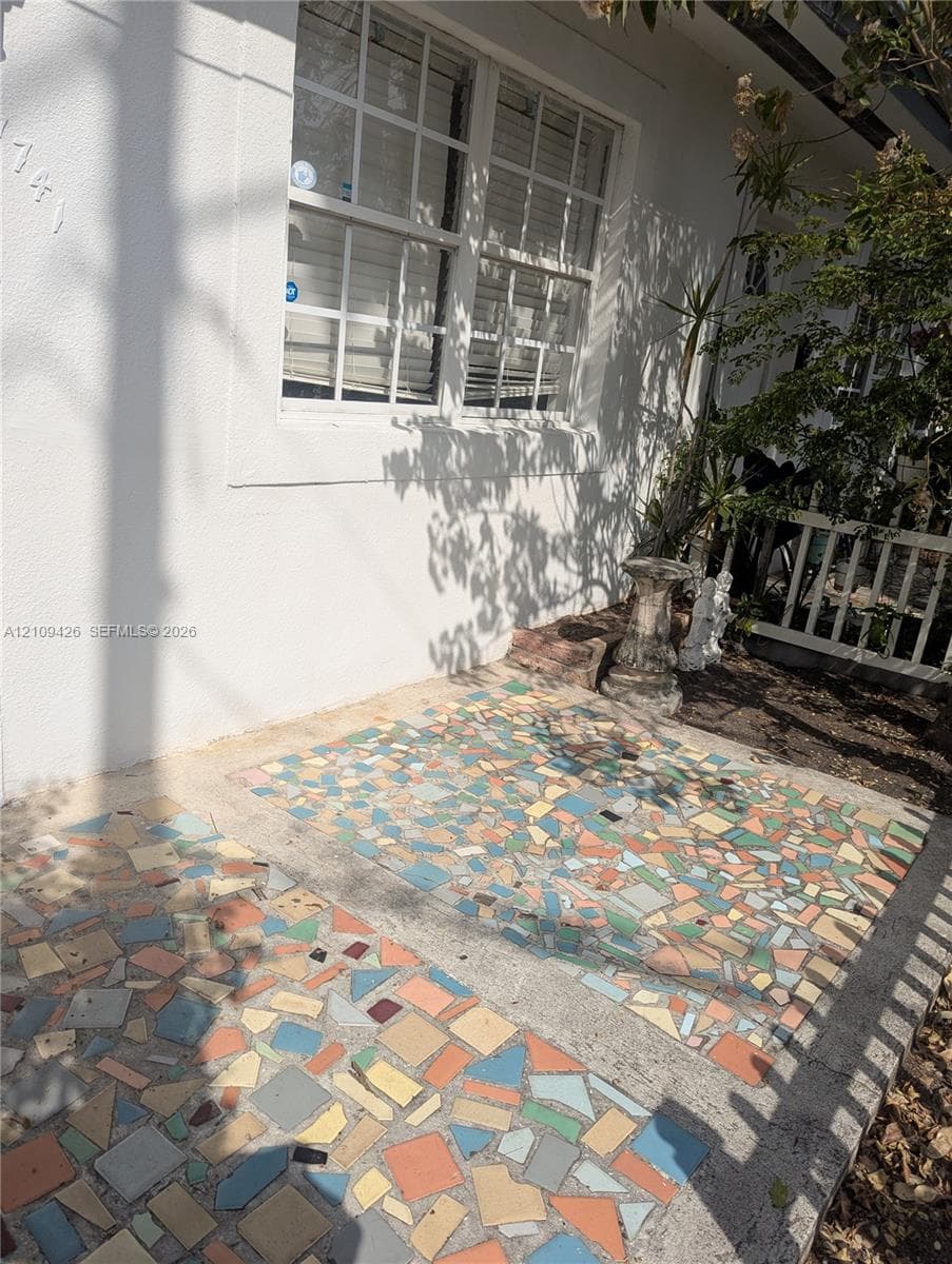 Stucco exterior featuring multi-colored mosaic tile patio flooring and a multi-pane grid window