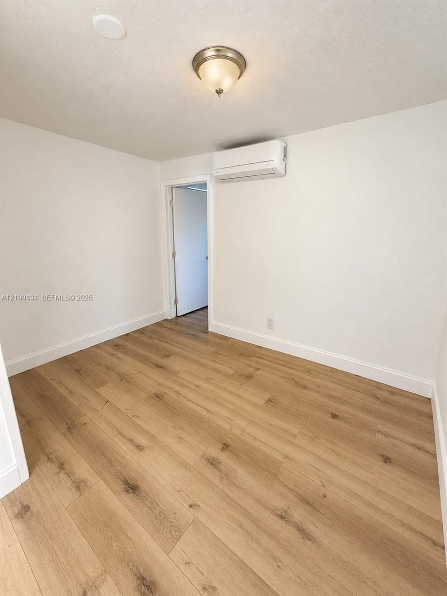 Room featuring wood-finish flooring, a wall-mounted ductless heating and cooling unit, and a ceiling-mounted flush-mount light fixture