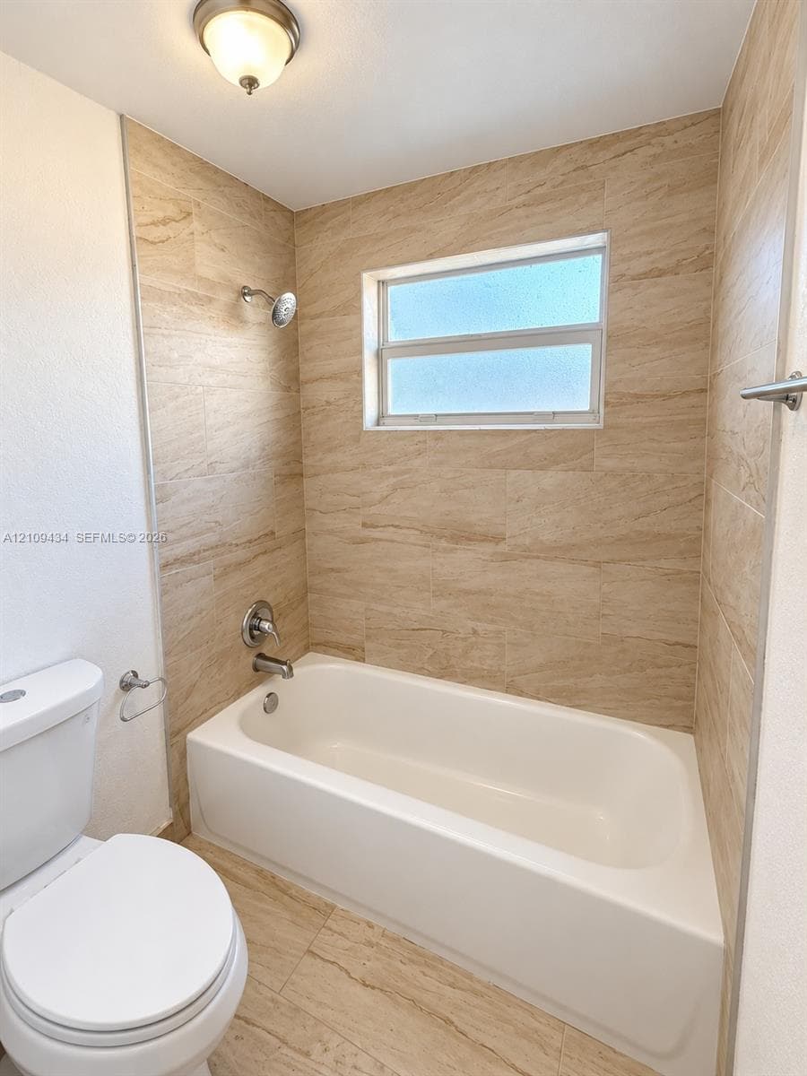 Full-size soaking tub featuring floor-to-ceiling tile surround with earth-tone finish, single-handle chrome plumbing fixtures, and an inset horizontal window