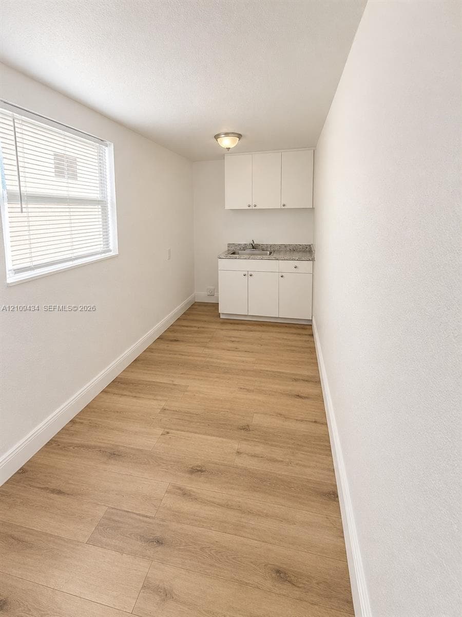 Wood-finish flooring, white built-in cabinetry, stone-finish countertop with integrated sink, and flush-mount ceiling lighting