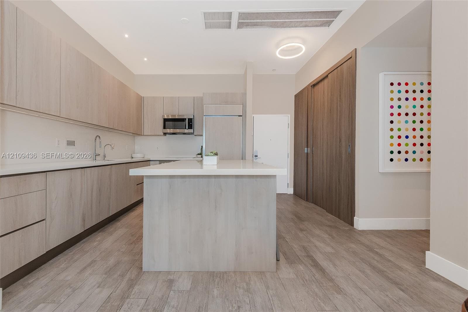 Kitchen featuring wood-finish cabinetry, stone-surface countertops, an integrated island, stainless steel appliances, and wood-finish flooring