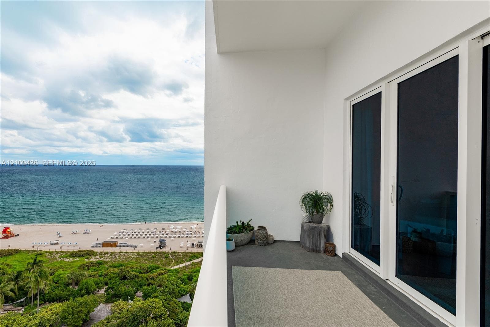 Covered balcony featuring concrete flooring, a white structural railing, and sliding glass panel doors