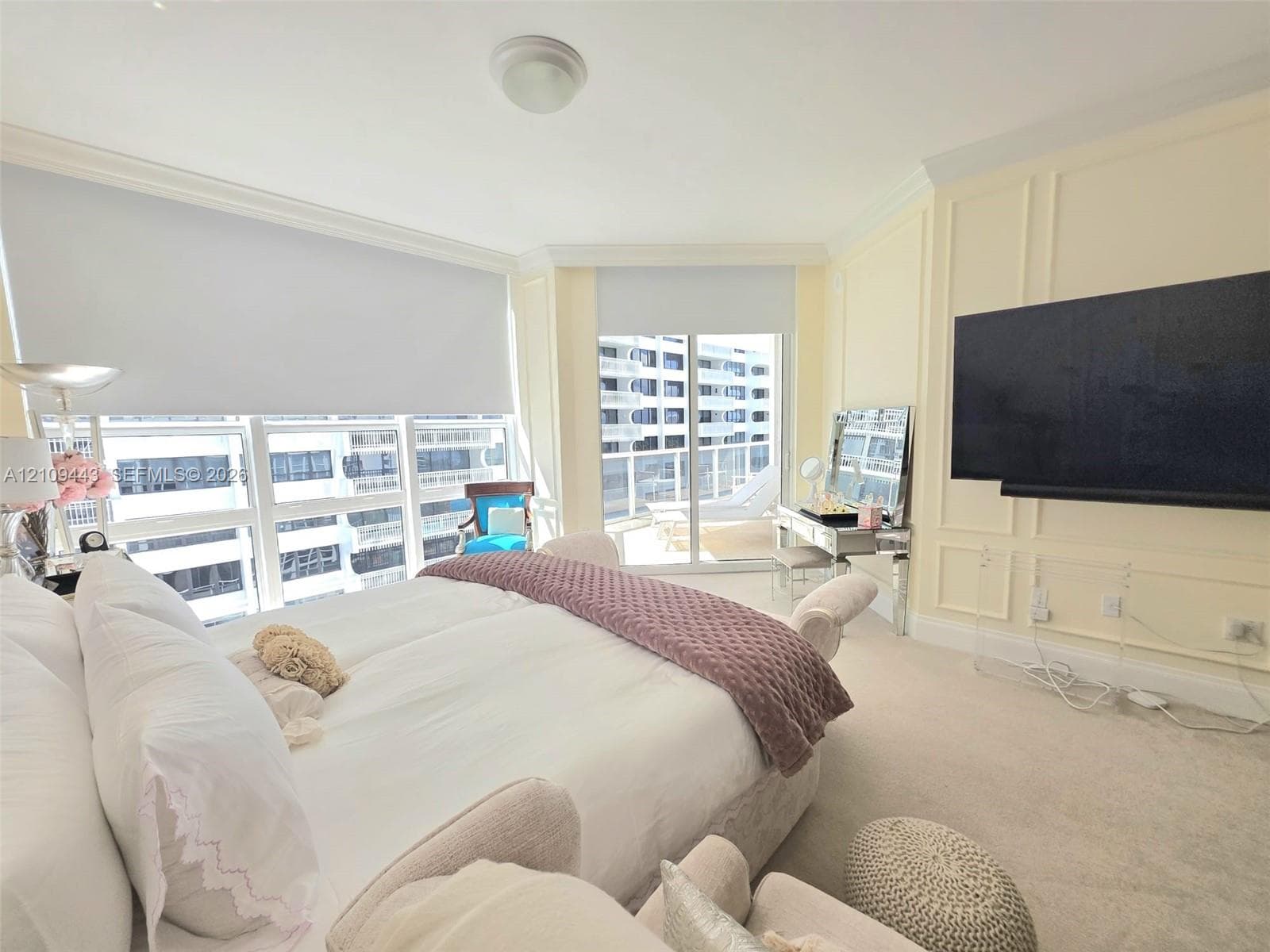 Expansive floor-to-ceiling windows, sliding glass door access to a private balcony, custom wall molding, neutral carpeting, and a ceiling-mounted light fixture