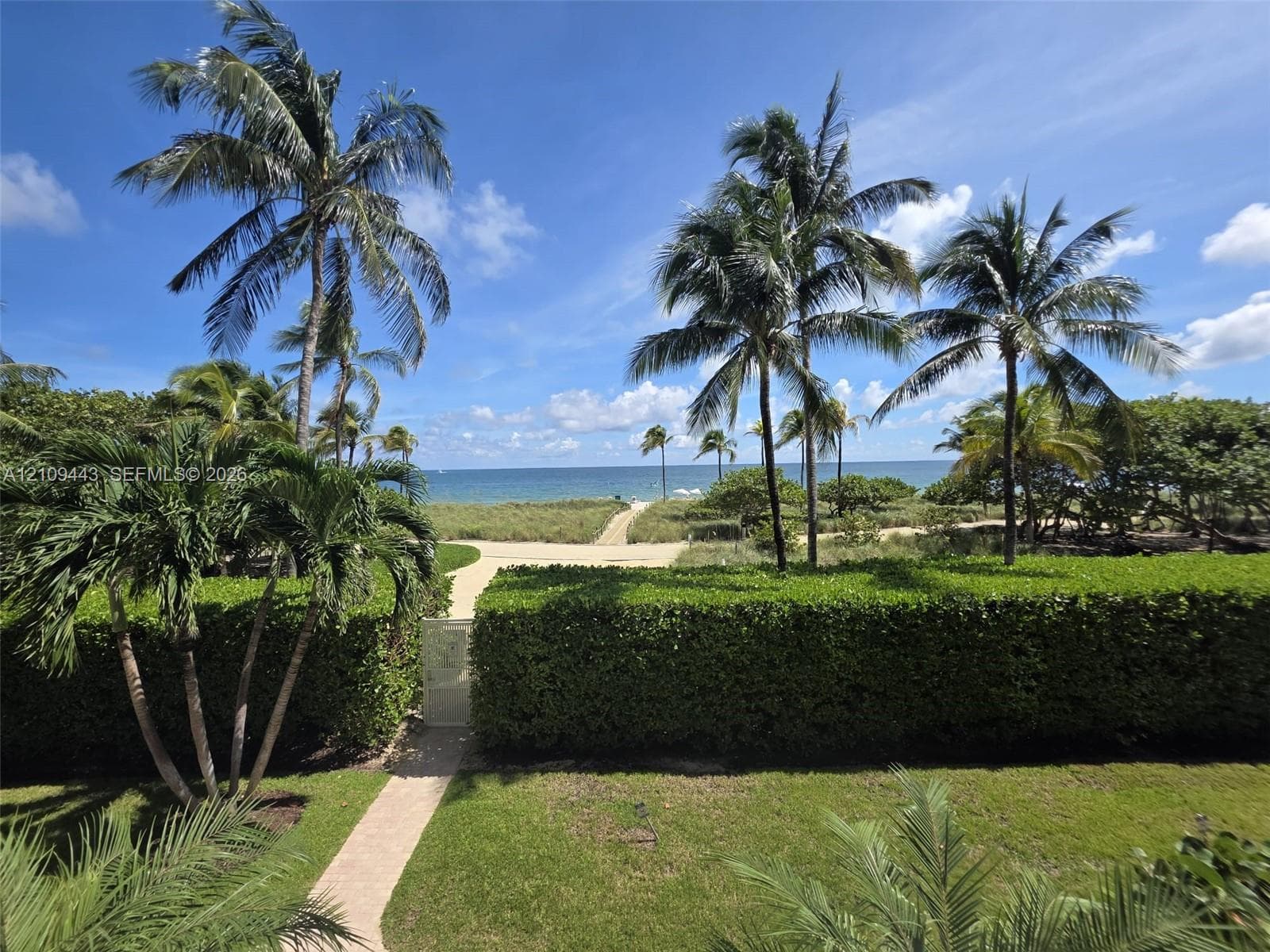 Manicured privacy hedges, mature palm trees, paved stone pathways, and open coastal water frontage