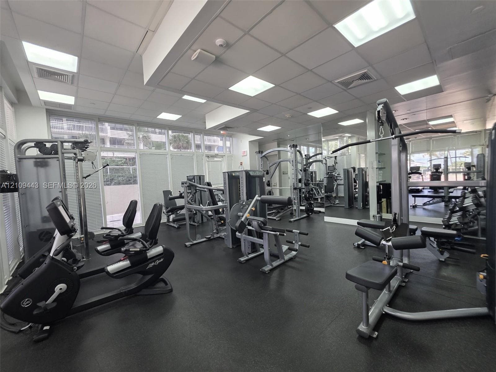 Fitness center featuring recessed square lighting, wall-to-wall mirrors, rubberized flooring, and expansive windows