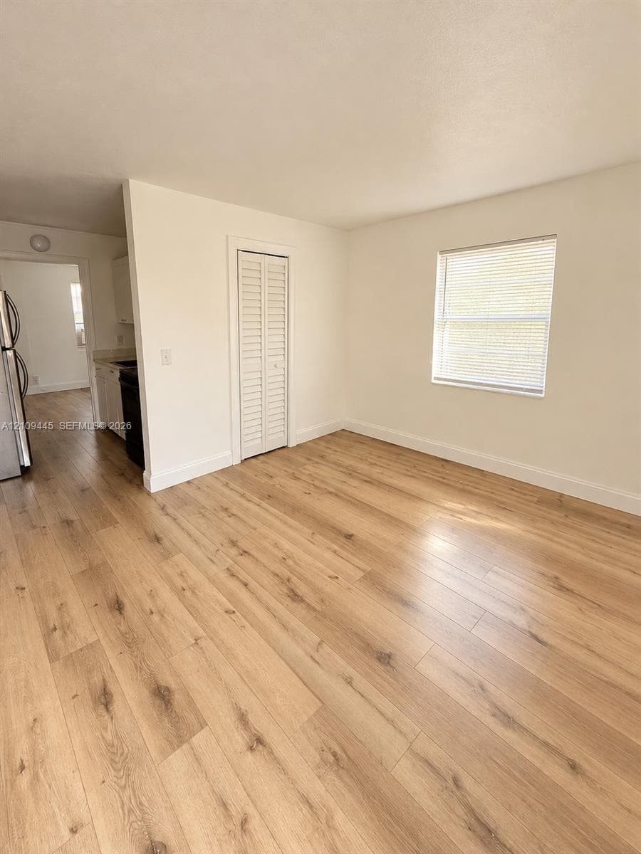 Interior space featuring wood-finish flooring, neutral wall tones, a single-window pane with blinds, and a built-in closet with bi-fold doors