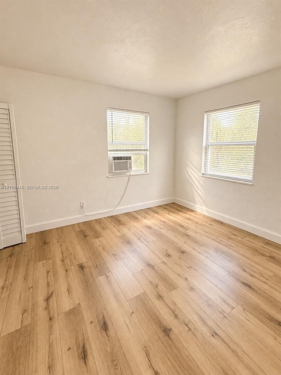 Interior space featuring wood-finish flooring, neutral wall tones, two windows with horizontal blinds, and a built-in closet with louvered doors