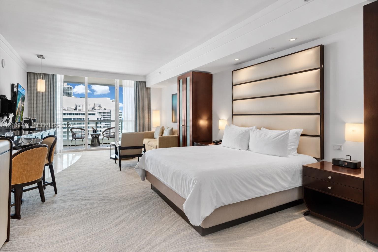 Full-height upholstered headboard featuring integrated lighting, custom dark-finish wood cabinetry, floor-to-ceiling glass sliding doors, and private balcony