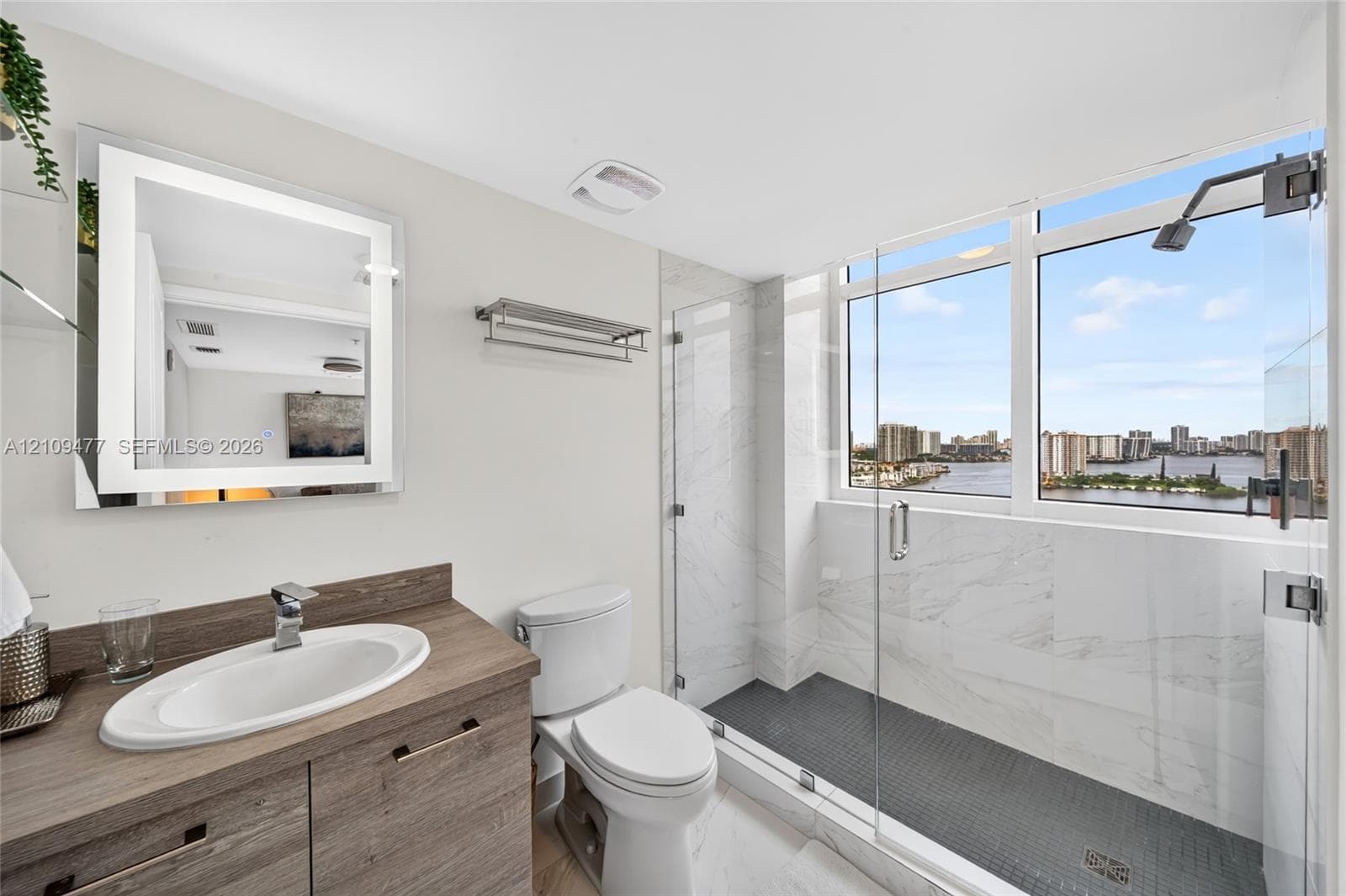 Living area featuring floor-to-ceiling glass doors, neutral tile flooring, flush-mount lighting, and exterior access to a balcony with water scenery