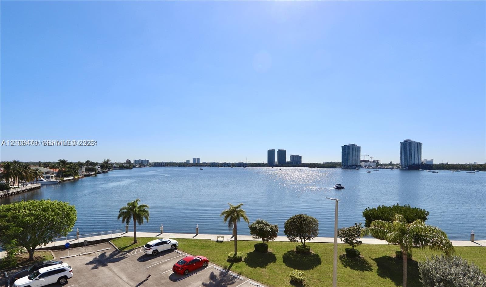Waterfront expanse featuring a concrete bulkhead, paved parking area, manicured lawn, and mature palm trees