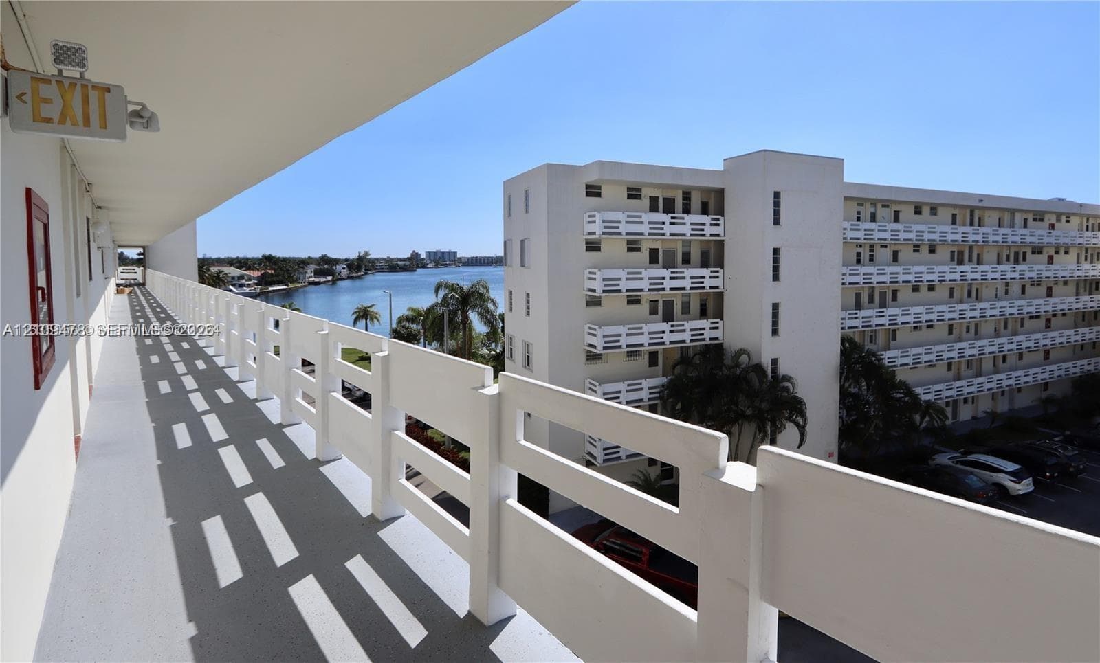 Exterior walkway with white horizontal railings, concrete flooring, and water scenery