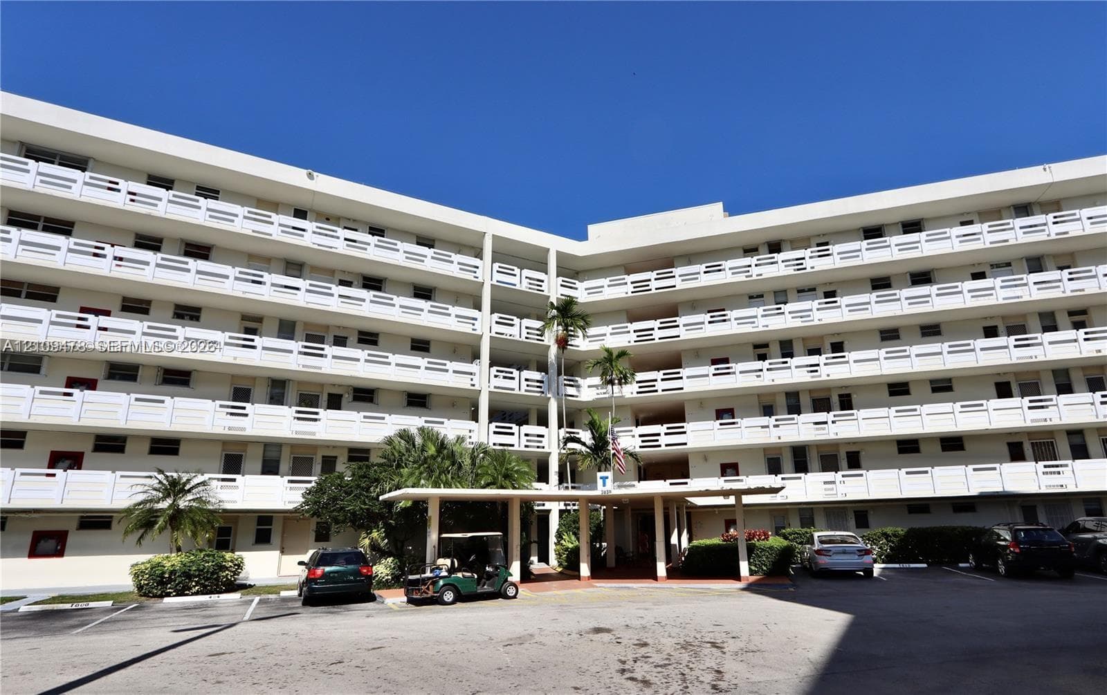 Multi-story building exterior featuring white concrete balconies with geometric railings and a covered porte-cochère entry