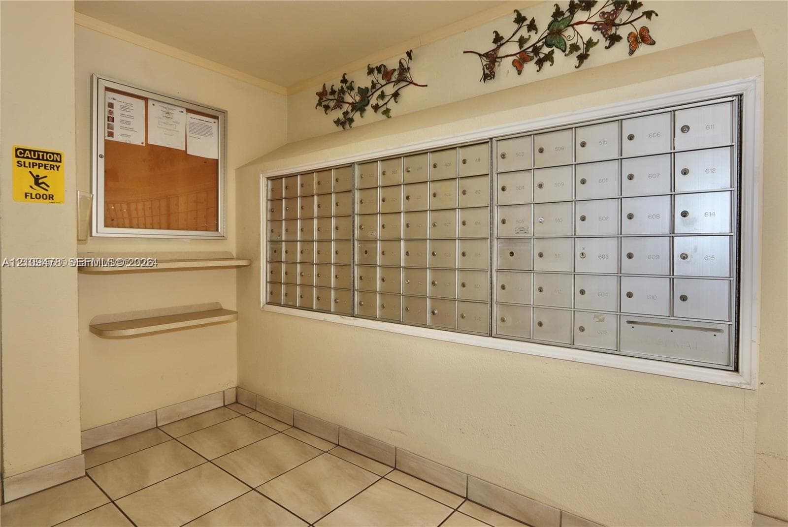 Wall-mounted metal mail distribution center featuring individual locking compartments, two integrated tiered shelves, and ceramic tile flooring