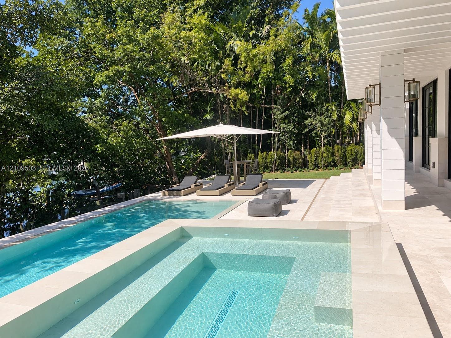 Custom-built swimming pool with integrated spa and stone-paved deck, sheltered by a covered patio with square columns and wall-mounted exterior light fixtures