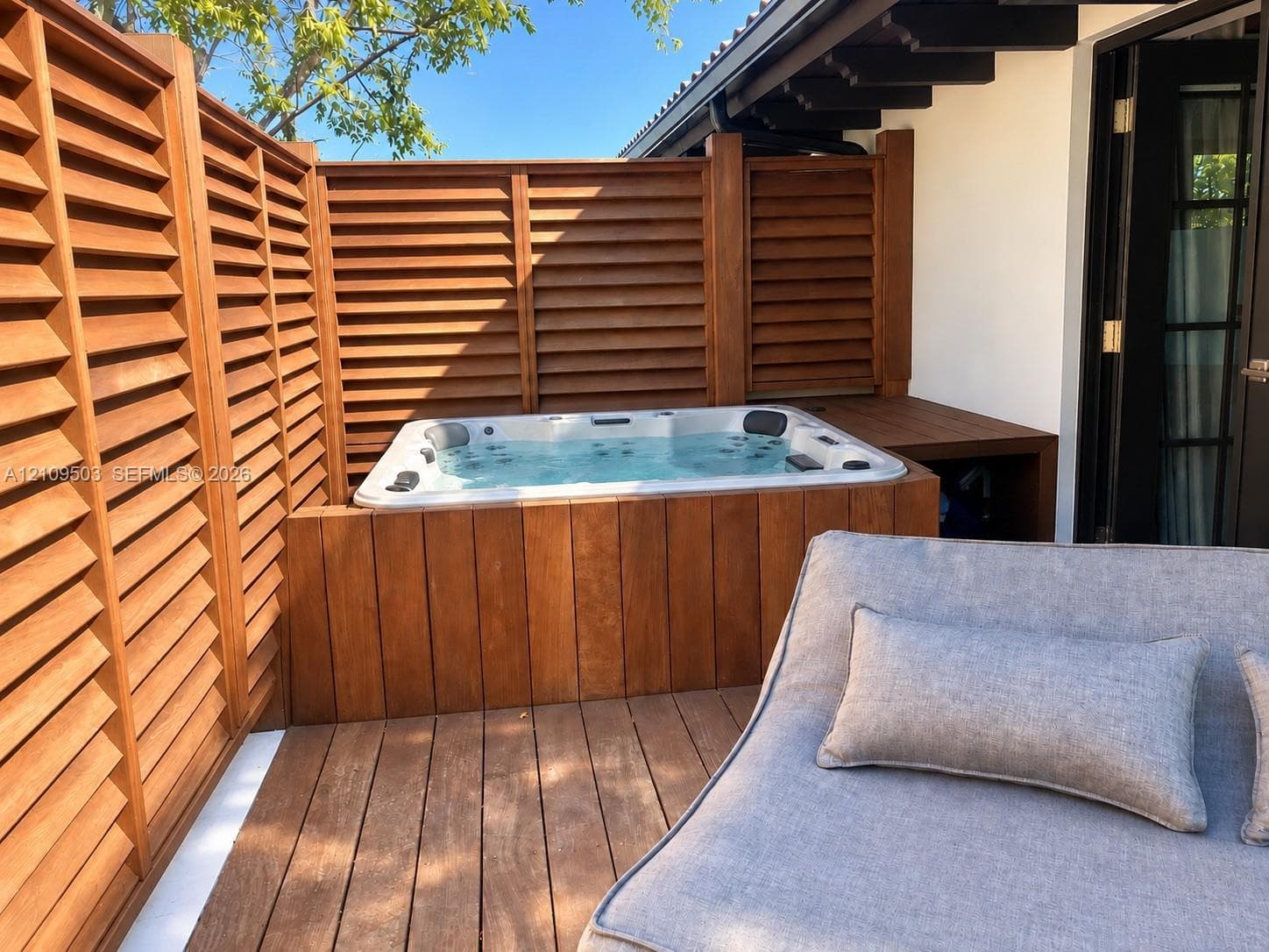 Private outdoor area featuring a built-in jetted spa, wood-finish decking, and slatted wood privacy screening