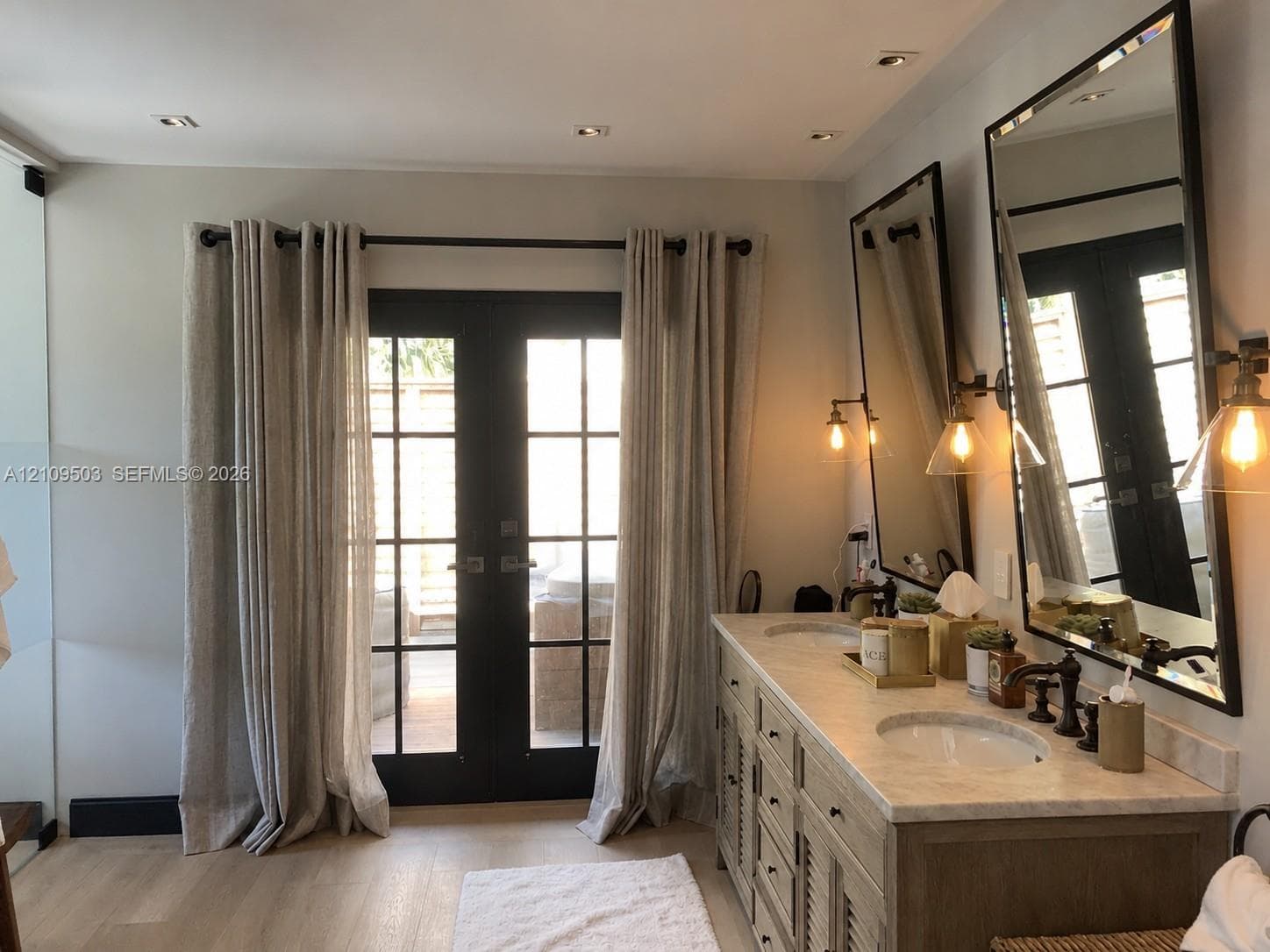 Dual-sink vanity with a stone countertop, recessed lighting, wood-finish flooring, and black-framed glass-paneled double doors