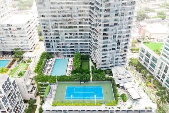 High-rise residential building featuring a blue-surfaced tennis court, swimming pool, landscaped lawn, and multiple levels of private balconies