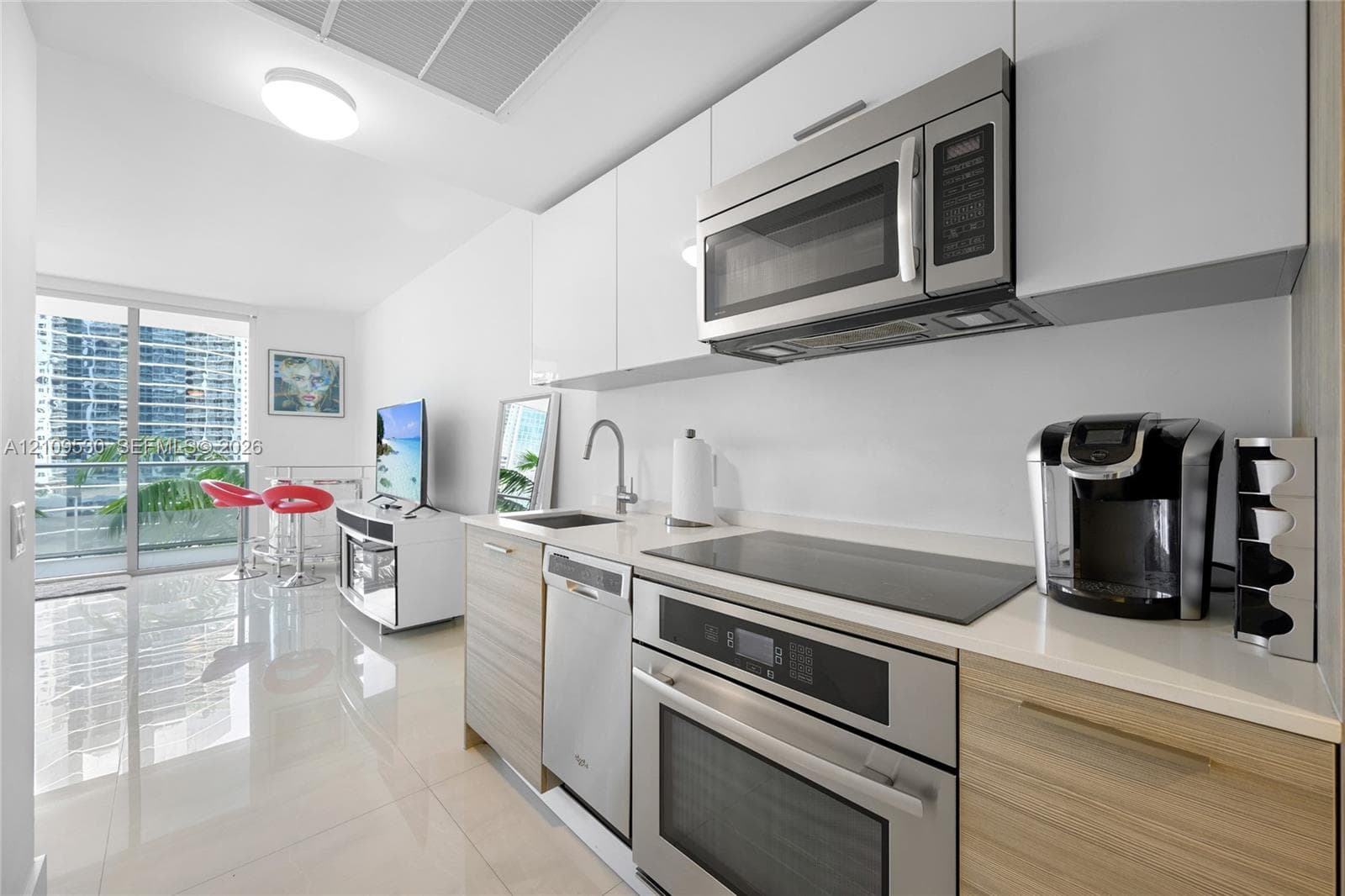 Kitchen featuring white gloss upper cabinetry, wood-finish lower cabinetry, solid surface countertops, stainless steel appliances, and integrated cooktop