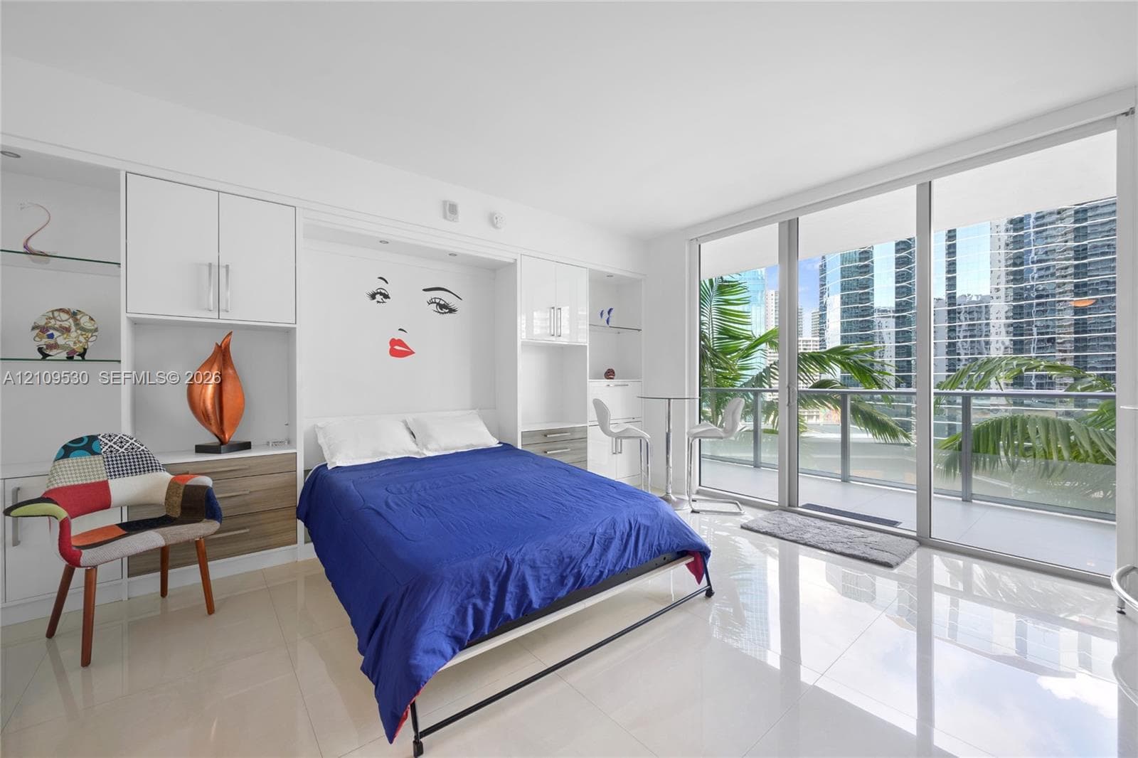 Floor-to-ceiling glass sliding doors opening to a balcony with glass railings, built-in floor-to-ceiling white cabinetry with glass shelving, and high-gloss tile flooring