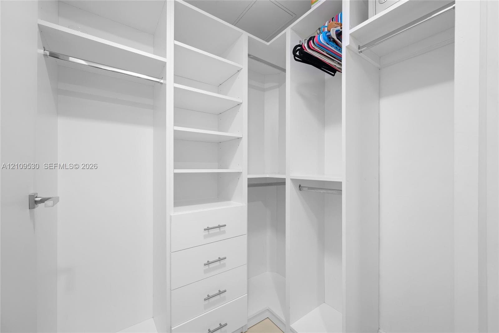 Custom walk-in closet featuring white built-in shelving, four integrated storage drawers with brushed metal pulls, and multiple tiered hanging rods
