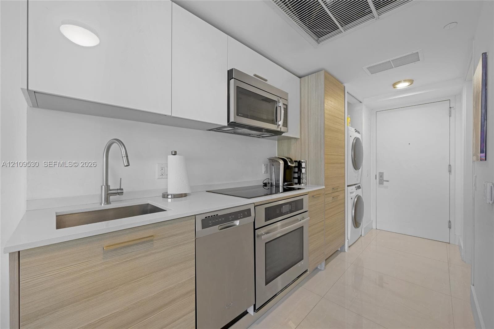 Kitchen featuring two-tone cabinetry with wood-finish lower cabinets and white upper cabinets, white solid surface countertops, stainless steel appliances, and tile flooring