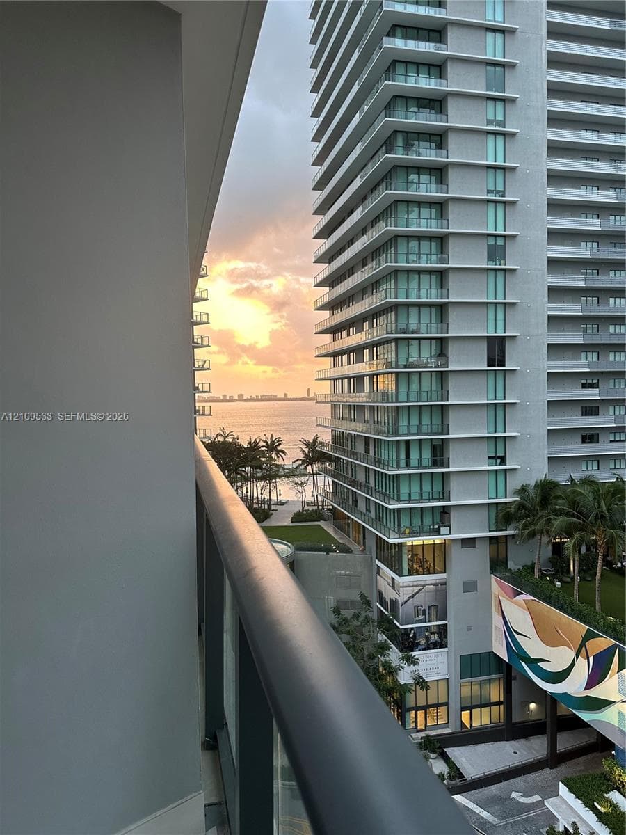 High-rise balcony featuring glass railings and panoramic water, skyline, and sunset scenery